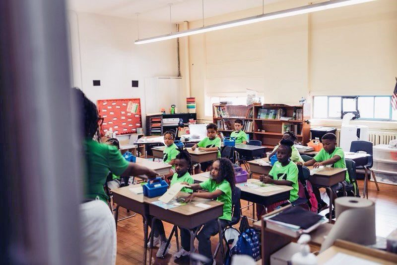 Teacher leading a lesson for students seated at classroom desks.